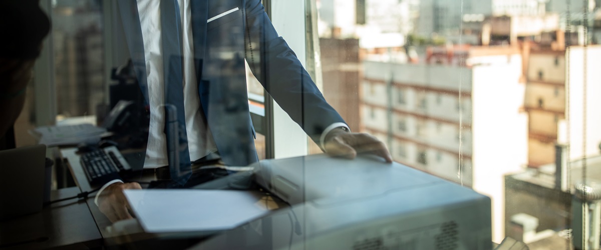 A businessman in suit using a printer in an office space.