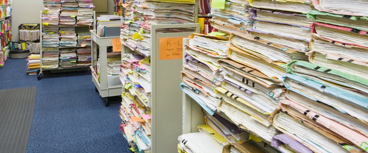 A library storage room with several shelves and pushcarts containing stacks of folders holding paper records and documents.