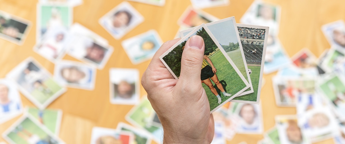 Man holds a few old trading cards in his hand with several trading cards spread out below him.