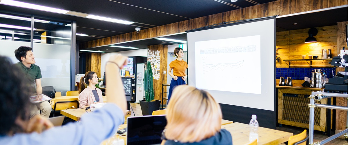 Coworkers hold a meeting in the middle of their workspace with a projector and screen.