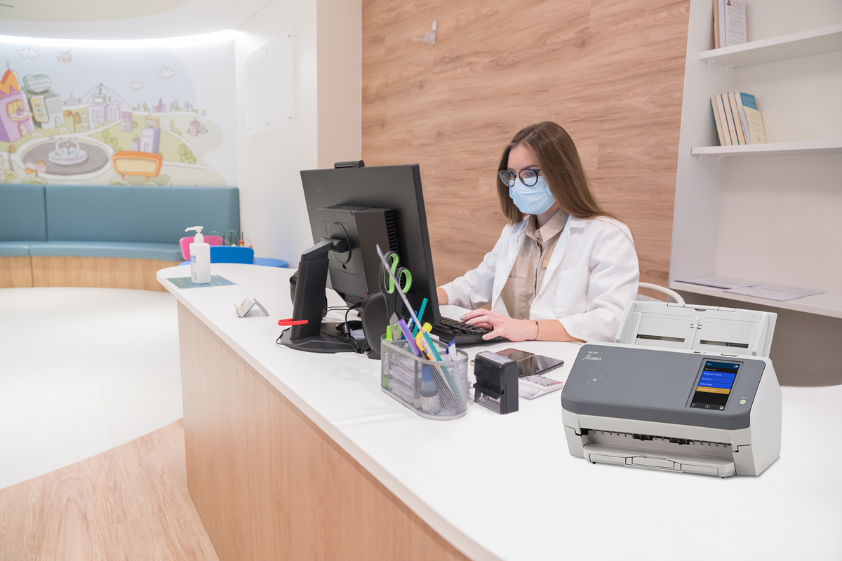 Health professional at a receptions desk in front of a computer with a fi-7300NX network document scanner.