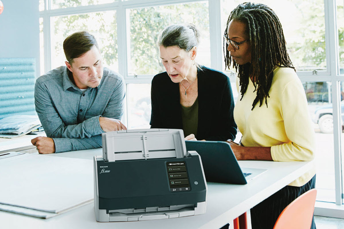 Office scene with two women and one man collaborating at a high des with a fi-8040 scanner. 