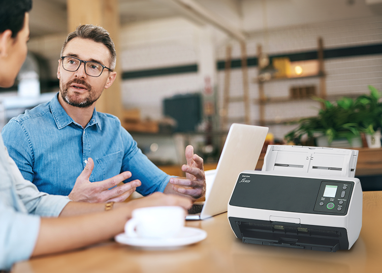 Two people having coffee at a table with with a Ricoh fi-8170 Document Scanner