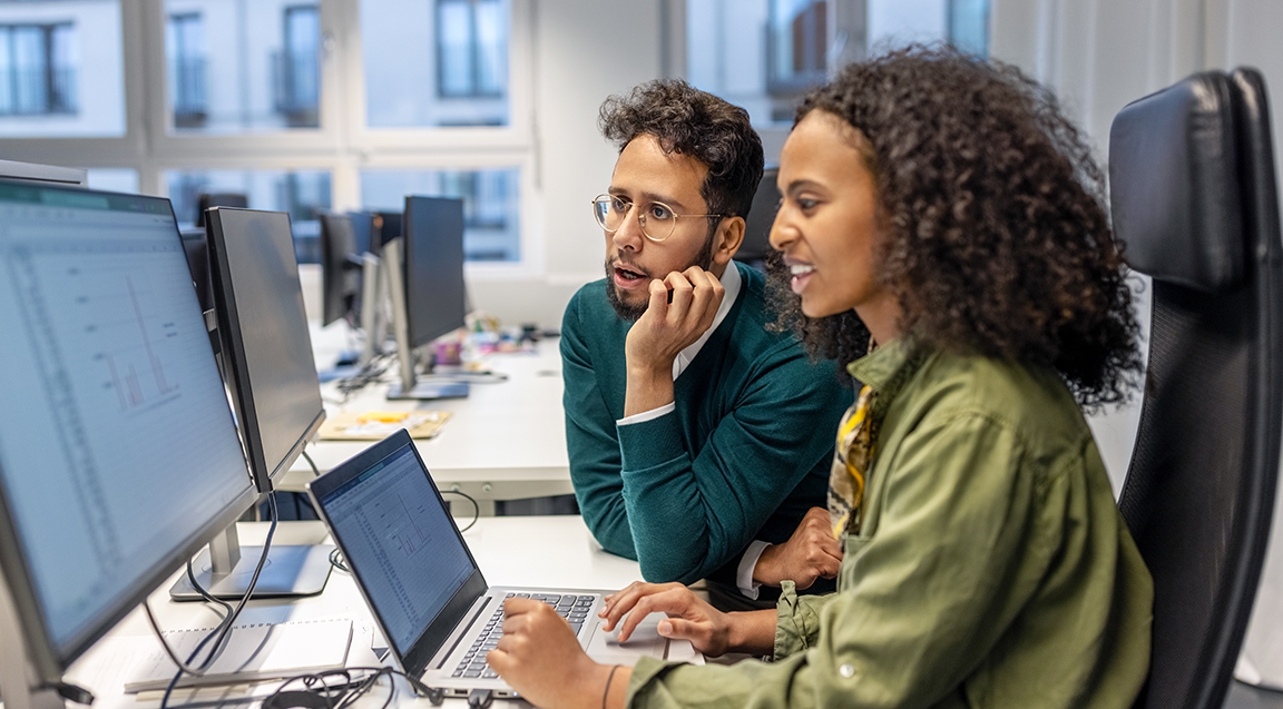 Image showing two people sitting at a desk reviewing something on a computer monitor.