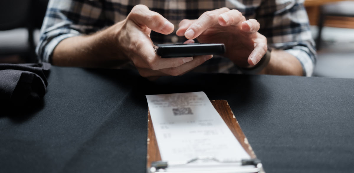 Person holding their phone over a receipt and taking a picture.